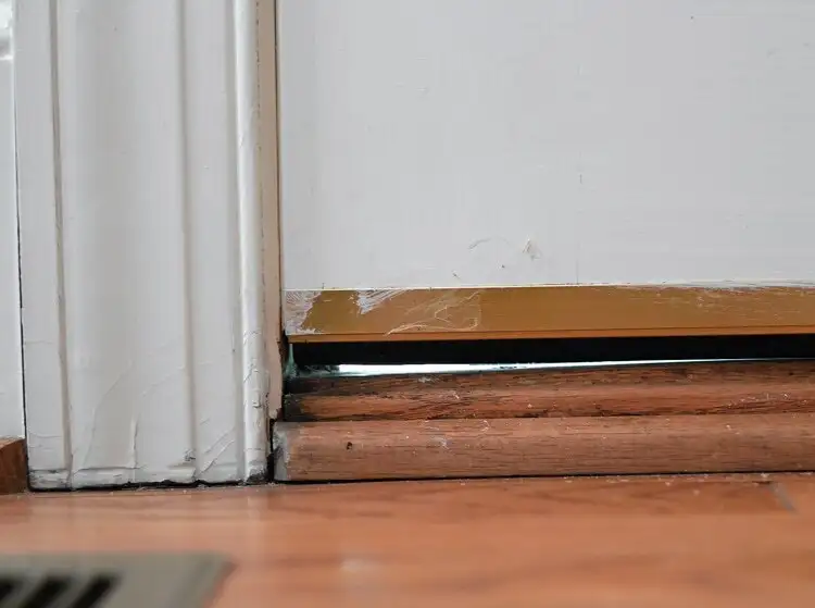 A small opening under the door where cool air escapes and heat comes in.